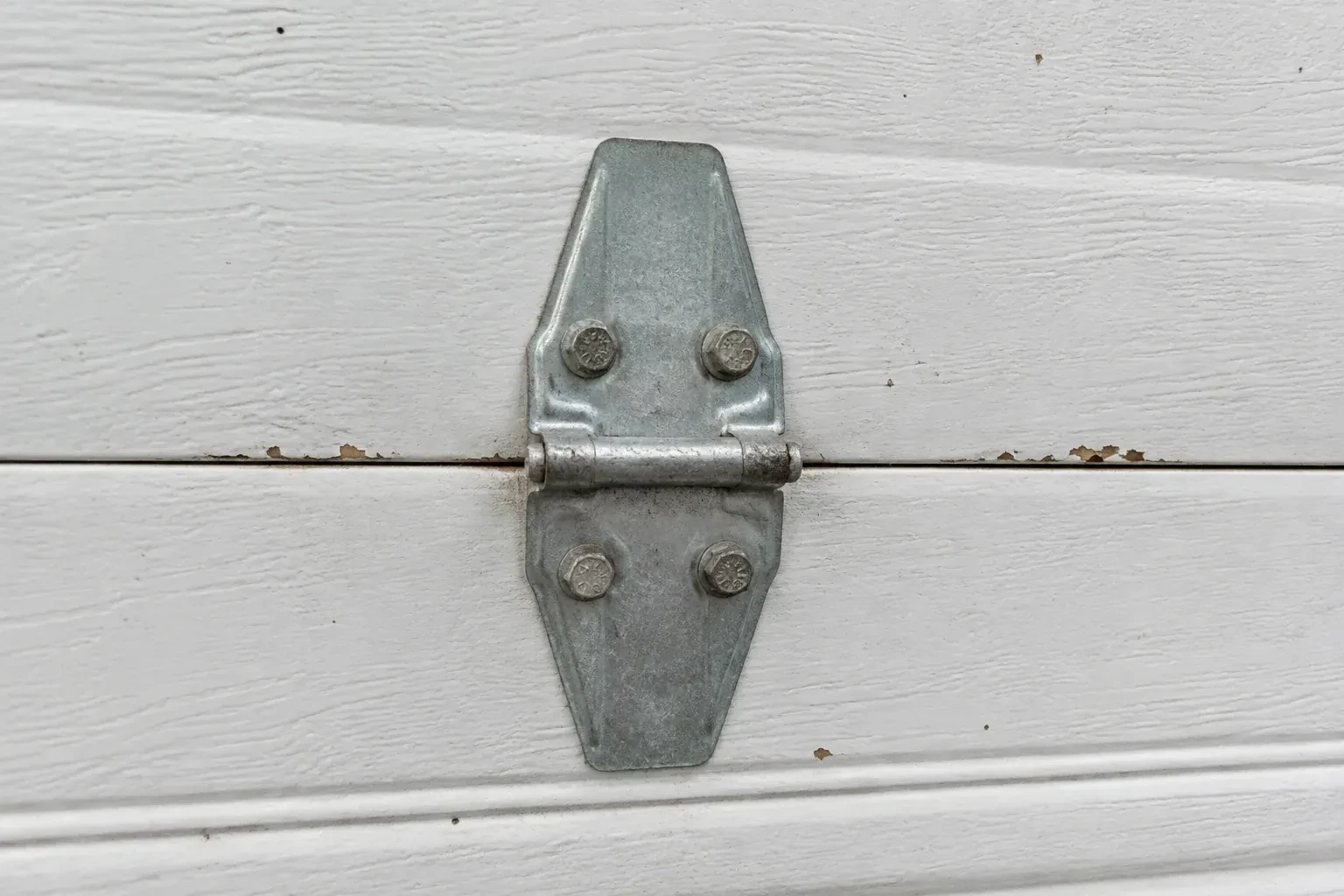 Metal center hinge across a seam in a white sectional garage door. — Garage Door Hinge Replacement, Guelph