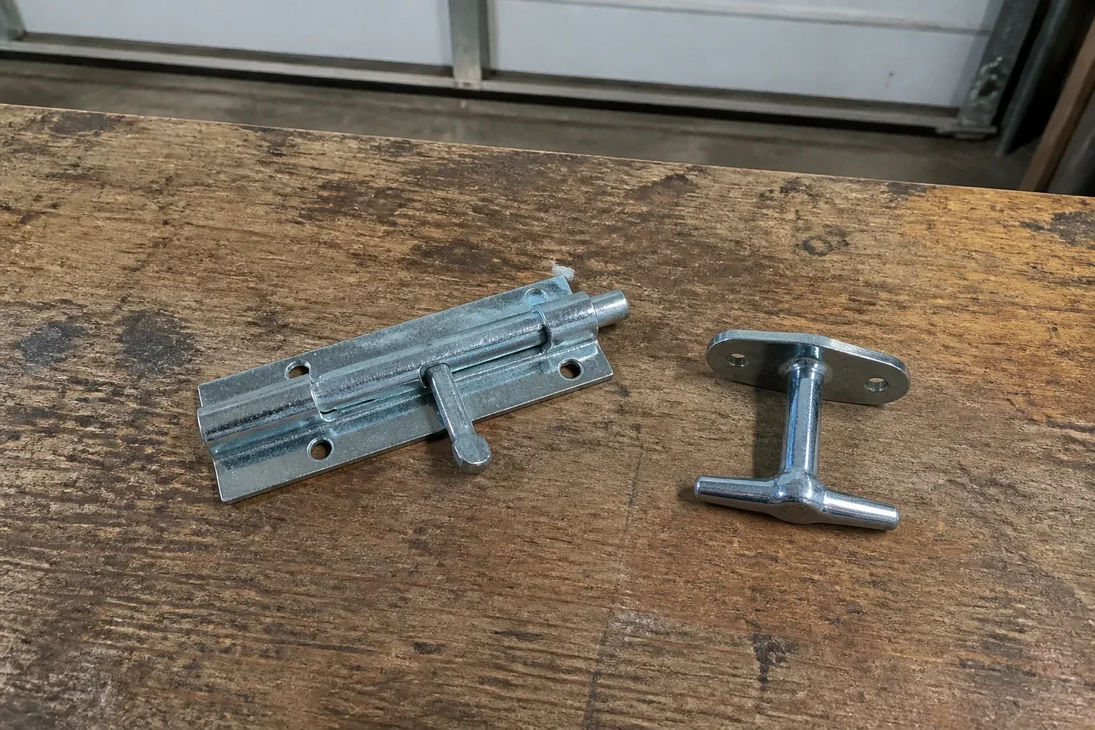 Detached slide bolt and T-handle on a wooden garage workbench. — Garage Door Manual Lock Repair, Guelph