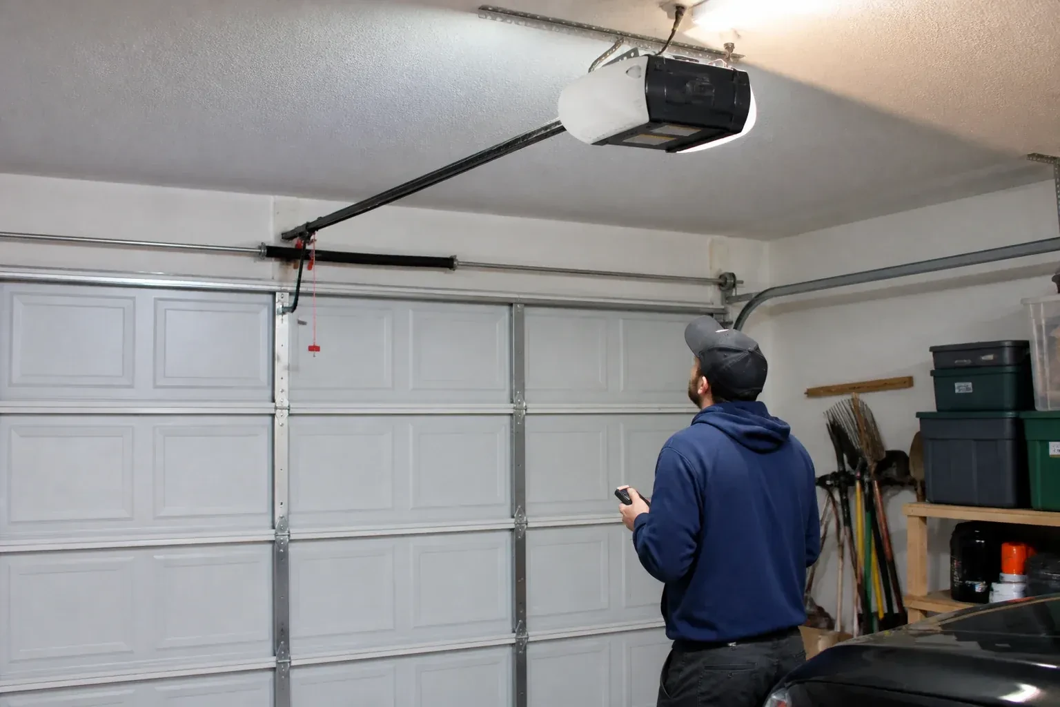 A person holding a remote looks toward an overhead garage-door opener and rail. — Garage Door Opener Diagnosis and Repair, Guelph