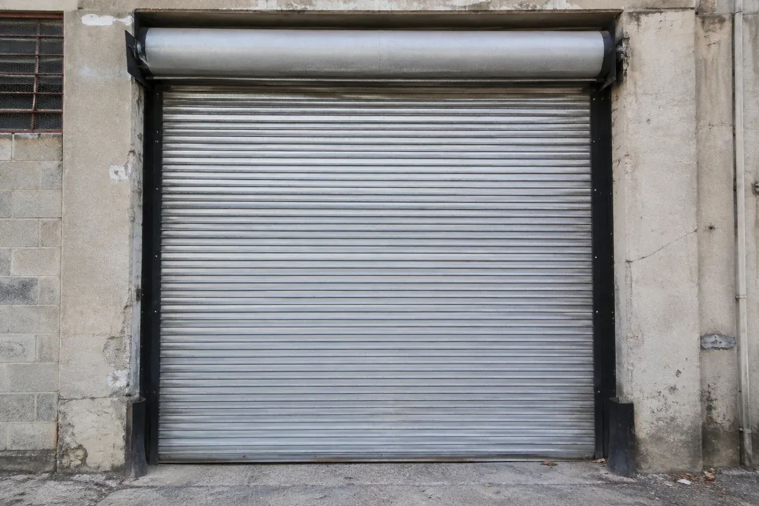 Closed metal rolling shutter in a weathered warehouse opening. — Commercial Rolling Door Repair, Guelph