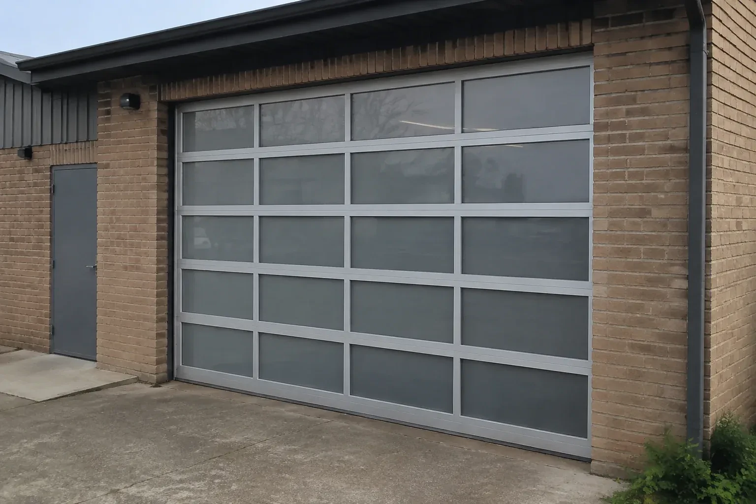 Closed glazed sectional door in a grey metal frame at a brick workshop. — Full-View Glass Garage Door Installation, Guelph