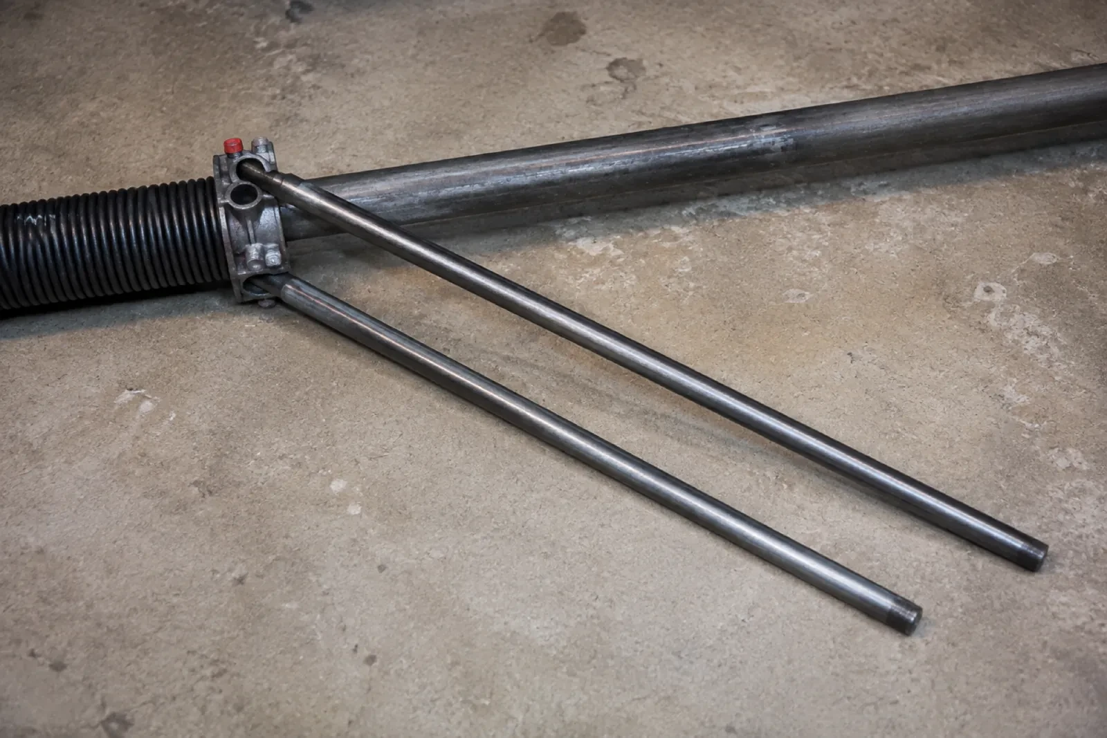 Two long steel winding bars inserted into the cone of a black torsion spring lying on a concrete floor.